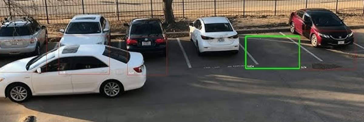 Real parking lot photo with OpenMV occupancy detection overlay marking occupied cars in red and an empty space in green